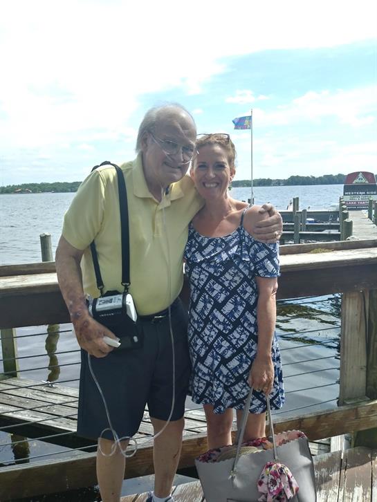 Two smiling individuals pose together at a dock on a sunny day, enjoying the pleasant weather.