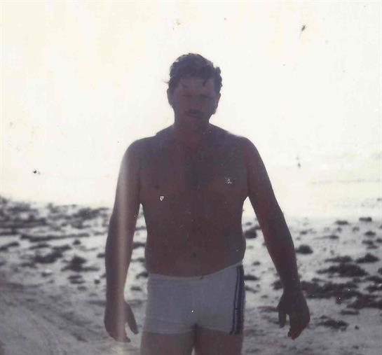 A man walks along the sandy beach as the sun sets, casting a soft glow over the water.