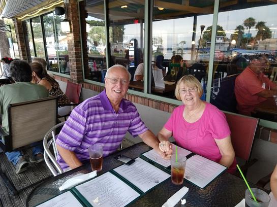A cheerful couple sits at an outdoor table, enjoying a meal and each other's company.