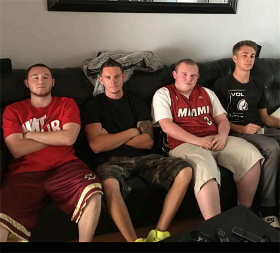 Four young men sit together on a couch, enjoying each other's company inside a living room.
