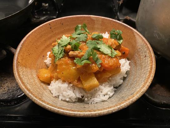 A hearty bowl of curry sits atop fluffy white rice, garnished with vibrant green herbs.