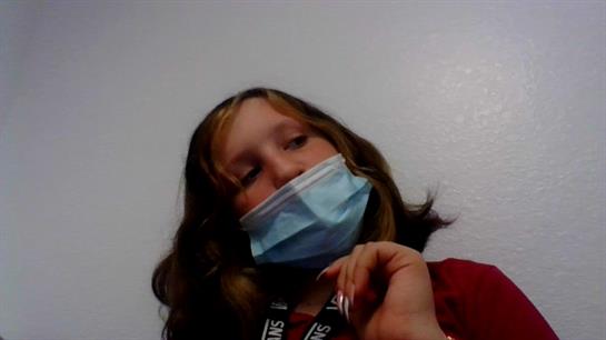 A child with brown hair and a blue mask appears deep in thought in an indoor space.