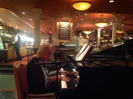 A pianist softly plays at a grand piano in a warm, inviting restaurant.