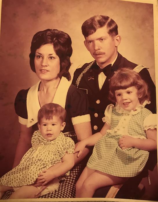 A couple poses in formal attire with two small children, reflecting a vintage family atmosphere.