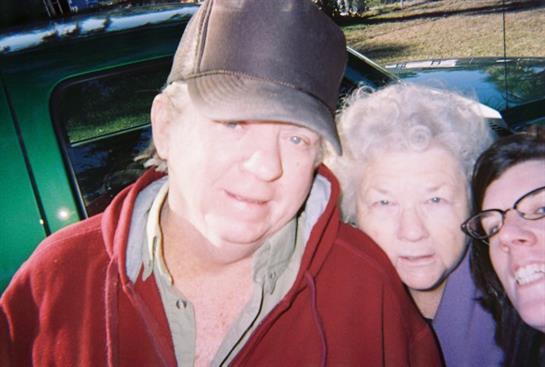 Pair of elderly individuals posing cheerfully, enjoying a social event in a natural setting.