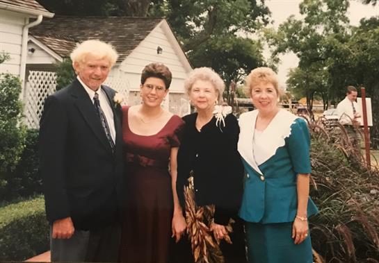 A group of four relatives stands together, smiling and dressed elegantly in a garden setting.