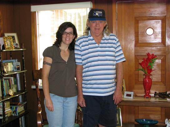 Two individuals stand together smiling in a comfortable wooden room decorated with various items.