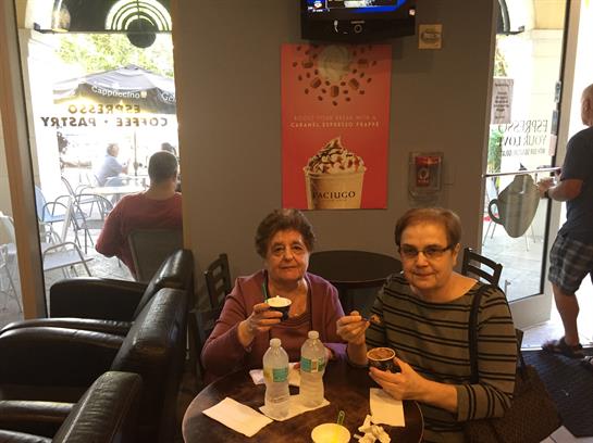 Two women sit at a table sharing desserts and refreshing water in a warm cafe atmosphere.