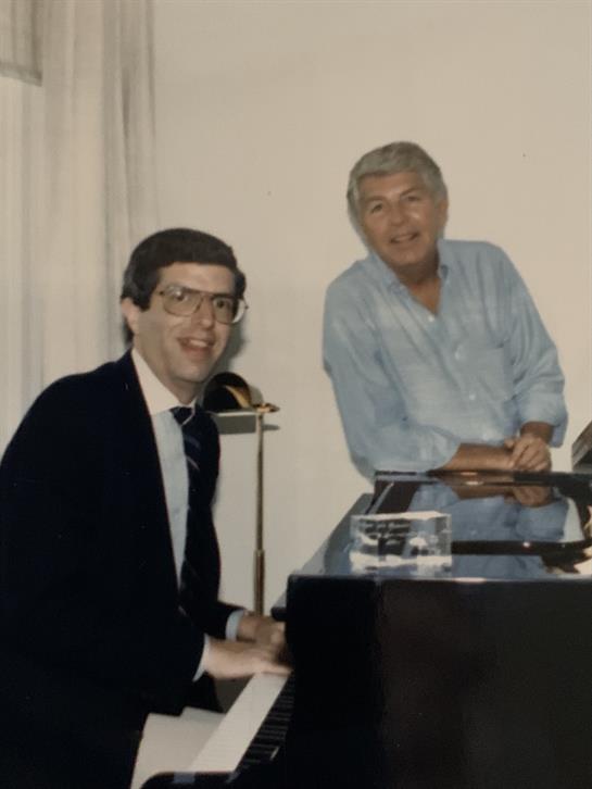 Two musicians enjoy a light-hearted moment at the piano in a comfortable indoor atmosphere.