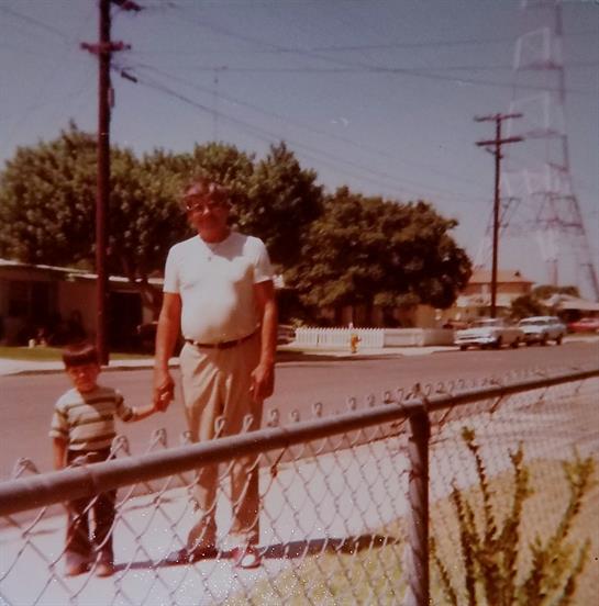A man and a boy stroll together, enjoying a sunny afternoon by the sidewalk in a quiet neighborhood.