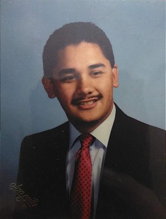 A young man dressed in a suit and tie displays a warm smile in a studio portrait.