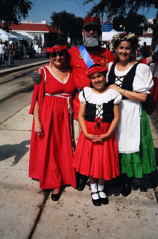 Three people in colorful traditional clothing pose at a cultural festival in daylight.