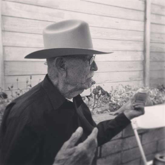 An elderly man animatedly shares stories with an attentive audience outdoors.