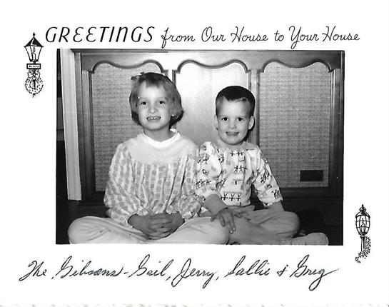 Two children pose together in their living room, smiling cheerfully for a festive greeting card.