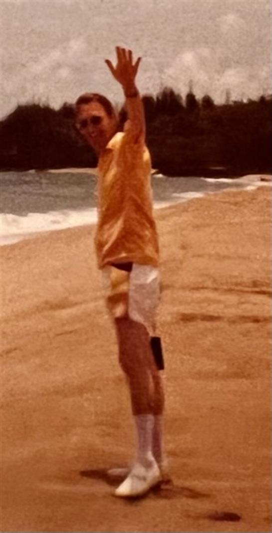 Young man wearing a yellow shirt celebrates on the sandy beach while the ocean waves crash nearby.