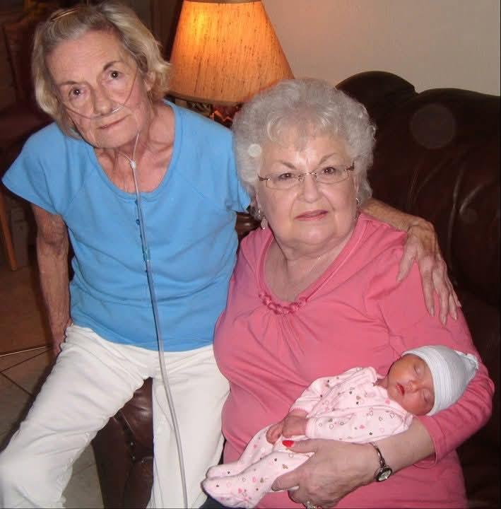 Elderly women smile while holding a newborn baby during a family gathering in a cozy living room.