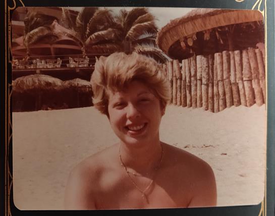 A smiling woman enjoys a sunny day at the beach surrounded by palm trees and a tropical setting.