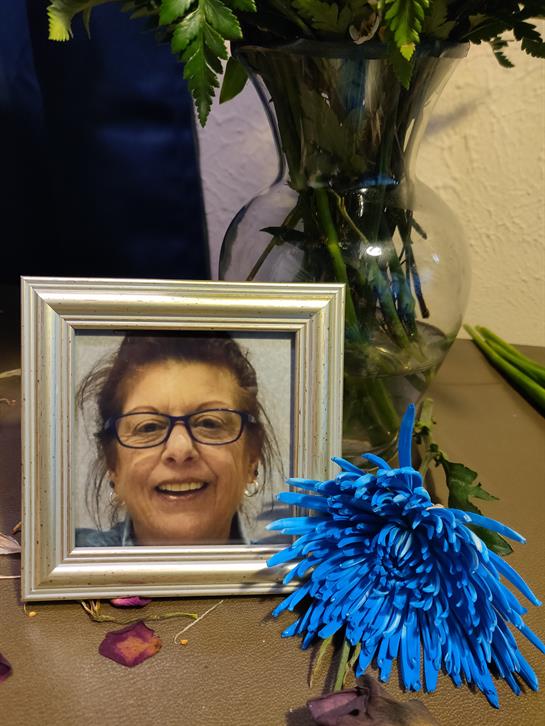 A framed picture of a smiling woman sits on a table surrounded by flowers and decorations.