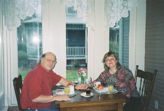 A couple shares breakfast at home, seated by large windows overlooking the garden.
