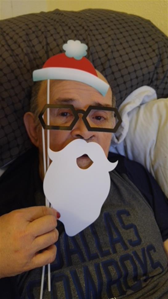 A senior man enjoys a cheerful moment, holding a festive Santa beard prop at home.