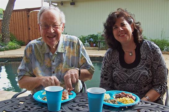 Two people share a meal by the pool, smiling and conversing in a relaxed setting.