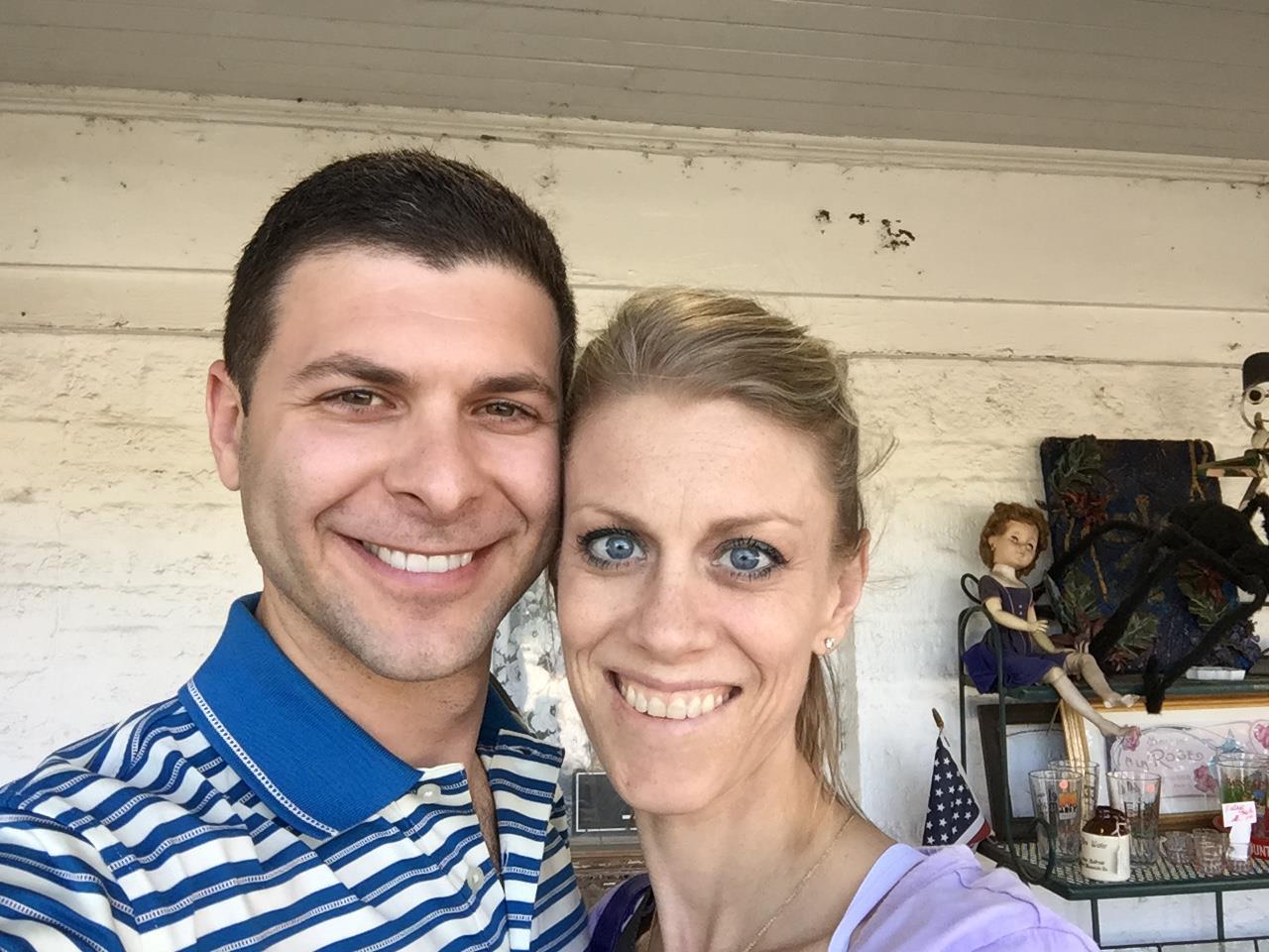 Smiling couple poses together at a quaint market filled with vintage items and rustic charm.