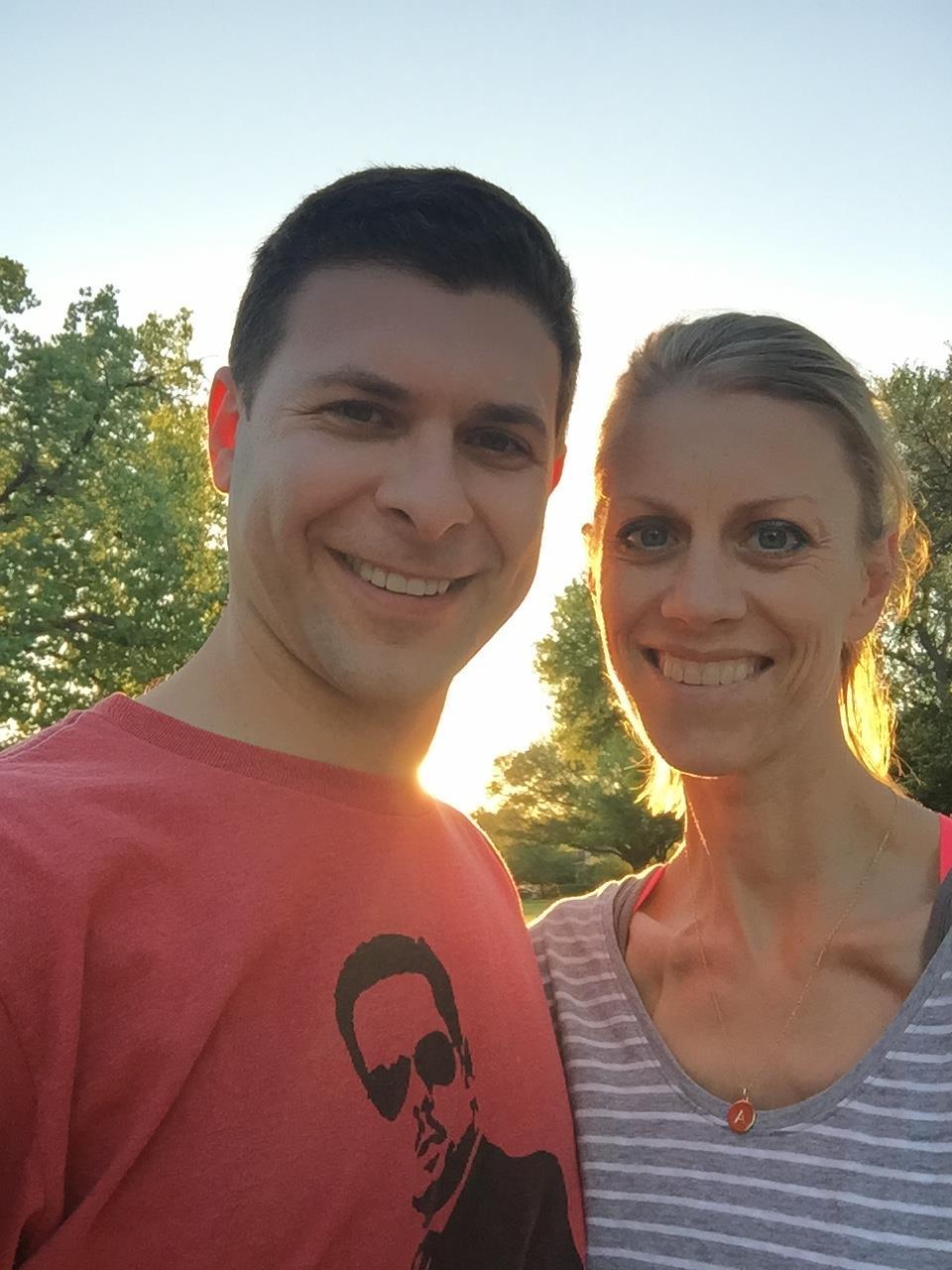 Two people smile together while basking in the warm glow of a sunset in a park.