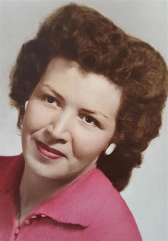 A woman with curly hair and pink lipstick smiles in a vibrant pink blouse.