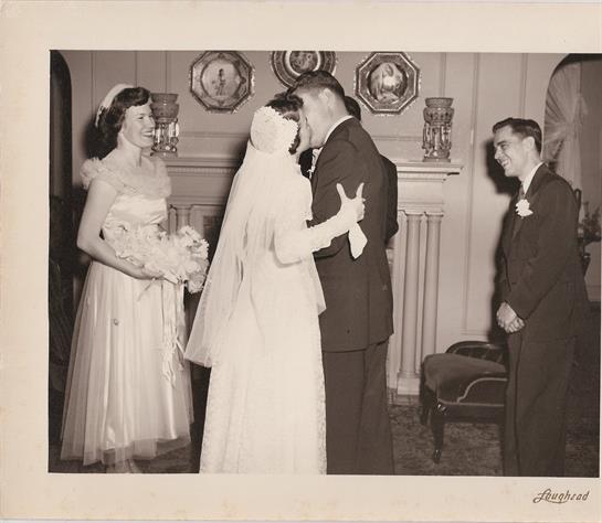Bride and groom share a tender kiss while guests celebrate in a graceful indoor venue.