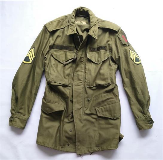 A light green military jacket with functional pockets and patches lies flat, showcasing its design.