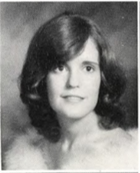 A young woman smiles gently, showing her curls in soft, 1970s-inspired lighting.