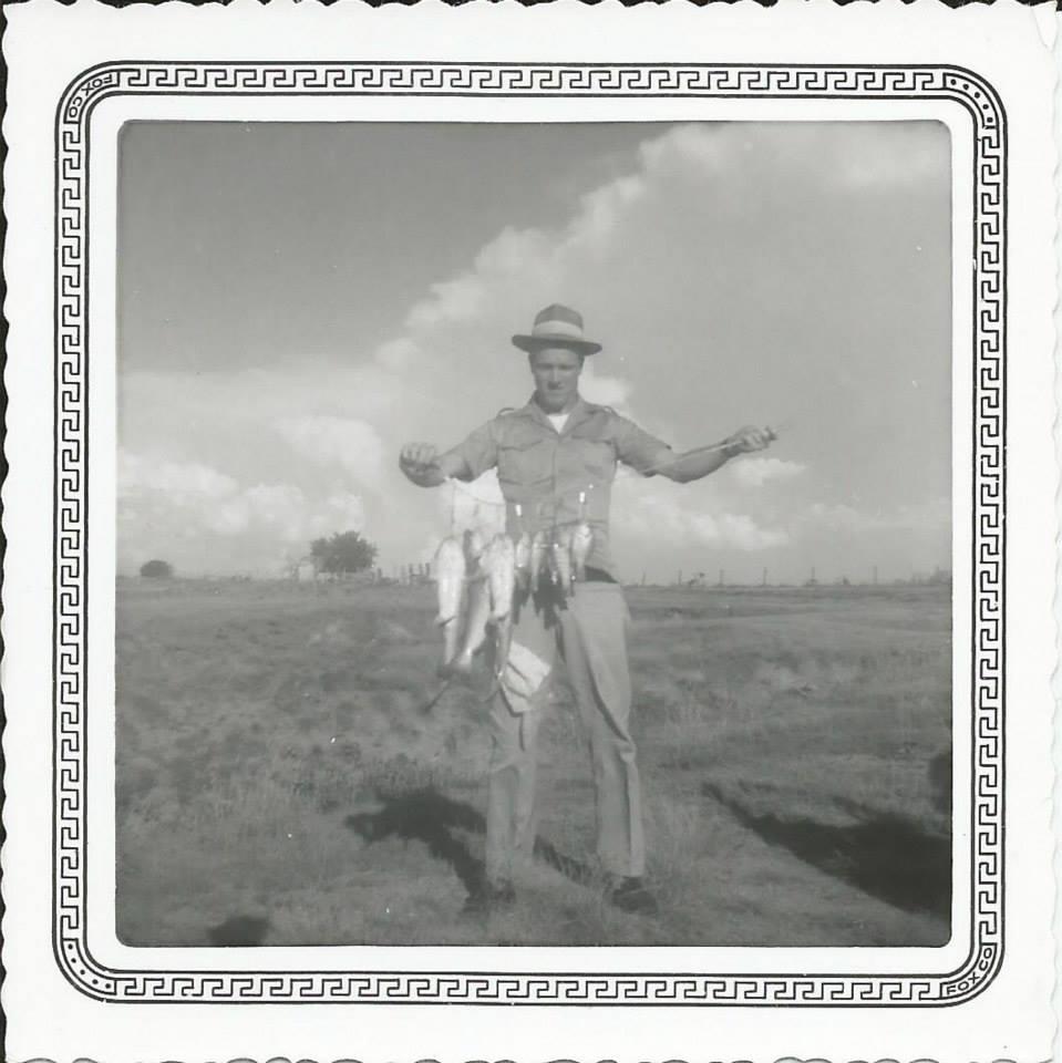 Fisherman holds multiple fish in hand, proudly showcasing his catch in an open field.