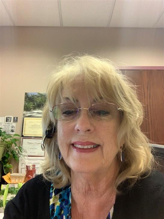 Woman communicates with a headset in a cozy office filled with plants and documents.