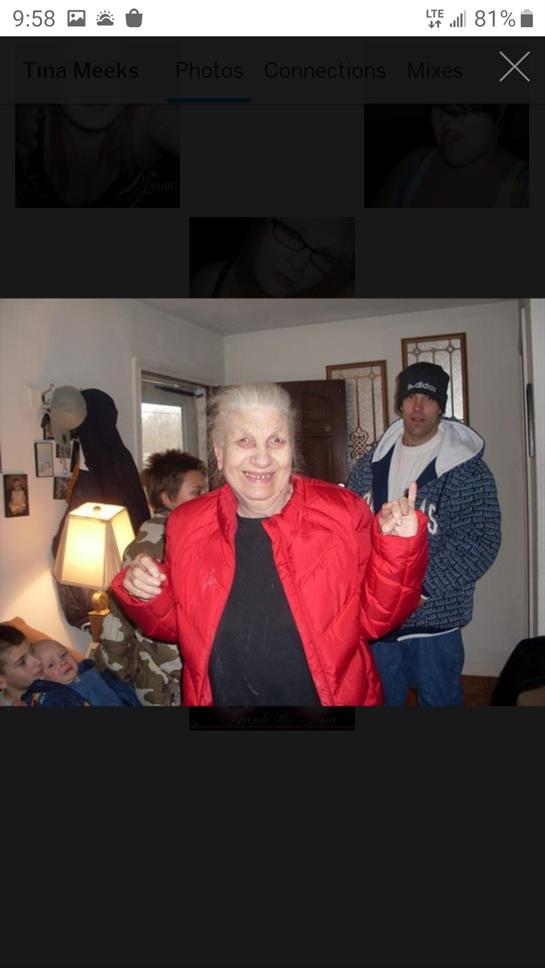 A cheerful woman in a red jacket dances with family members during a cozy indoor gathering.