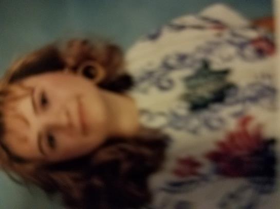 A young girl in a floral dress beams on a sunny day at the park.