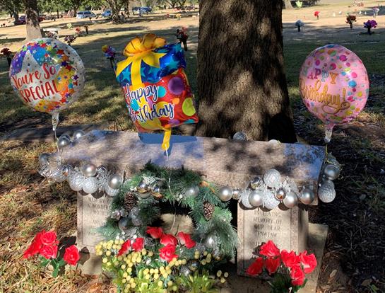 Colorful balloons and flowers are placed at a memorial site, creating a festive atmosphere.