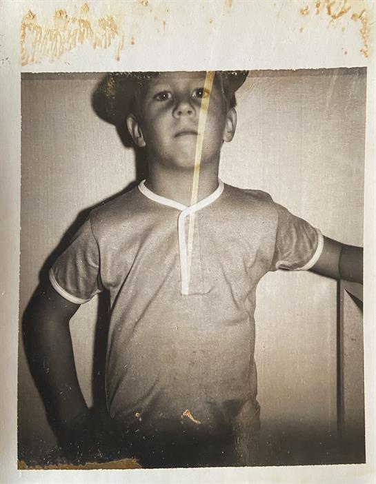 A young boy stands poised with a confident expression, wearing a hat and retro shirt.