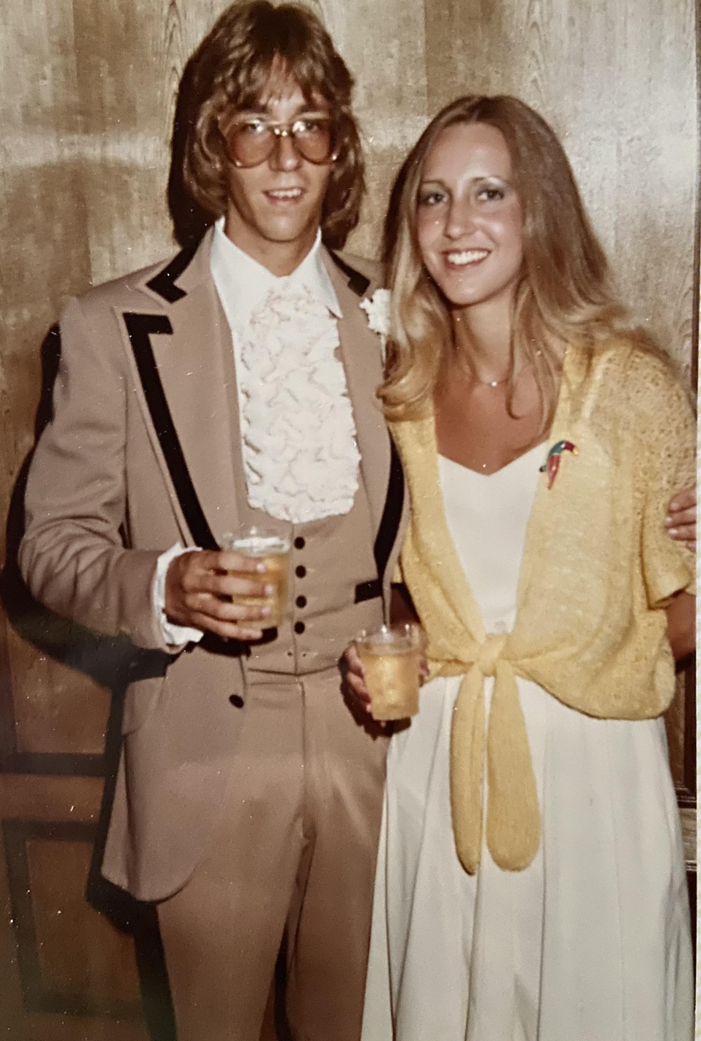Couple dressed in formal clothing enjoys drinks together at a celebration in a cozy setting.