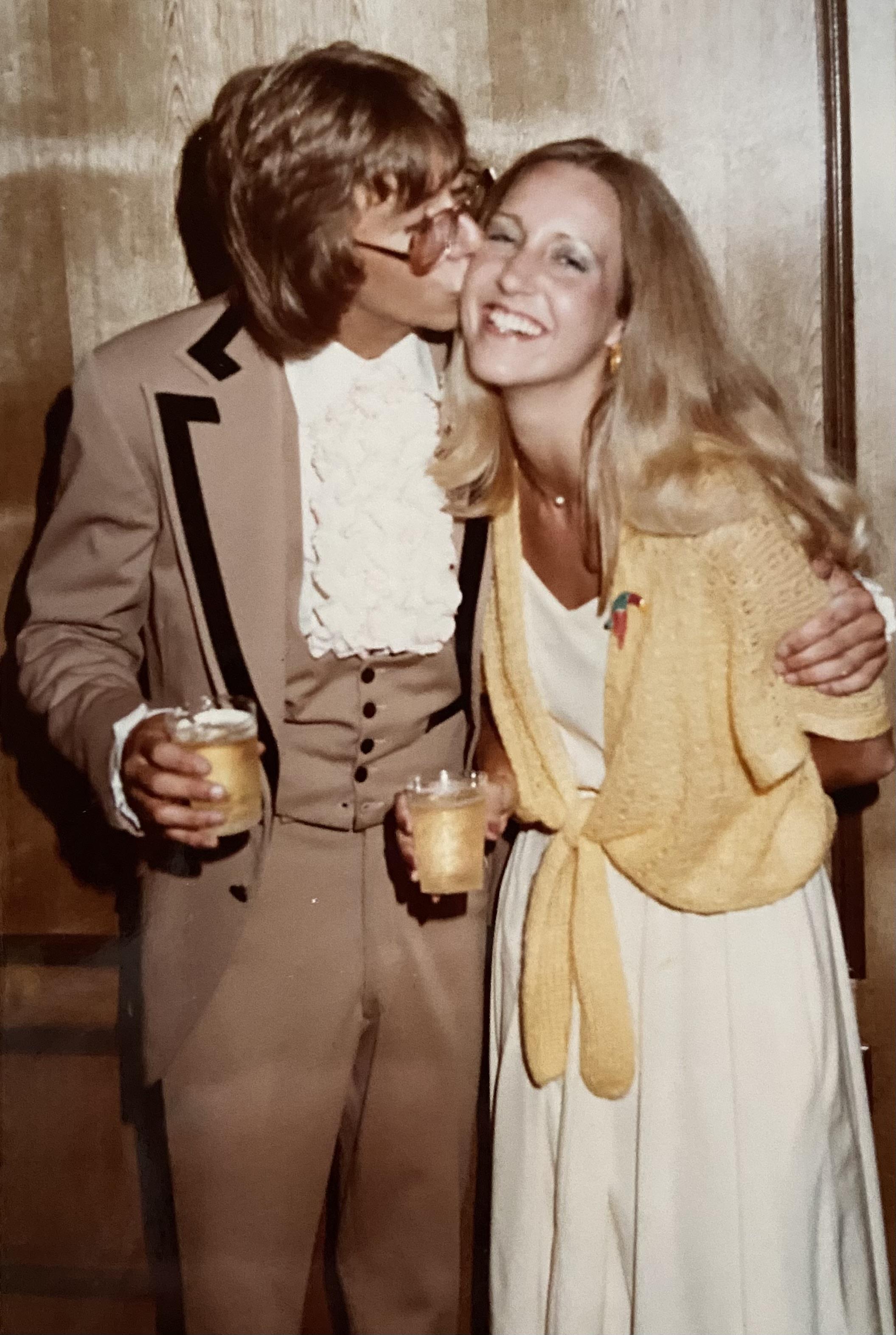 Two people embrace and share a joyful moment at a party, dressed in stylish vintage clothing.
