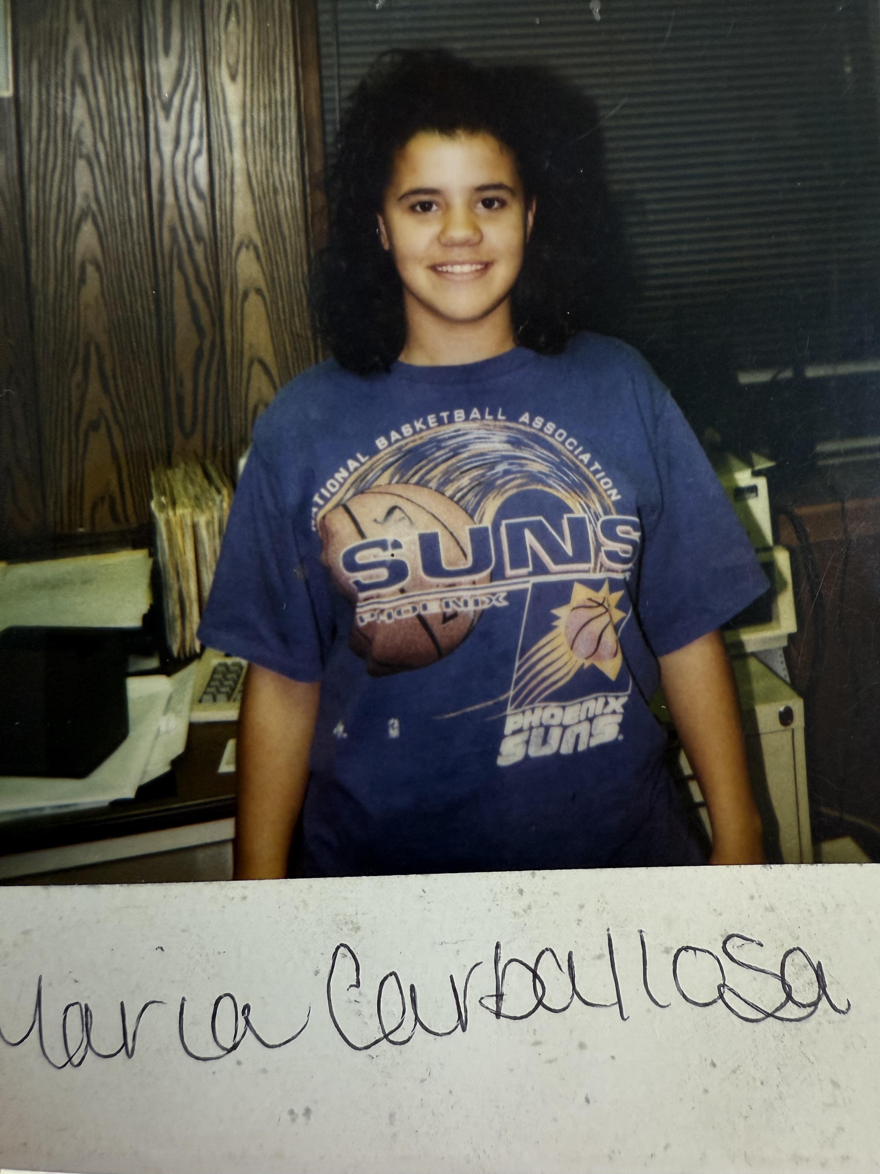 A young woman poses happily in a purple sports shirt, surrounded by office supplies.