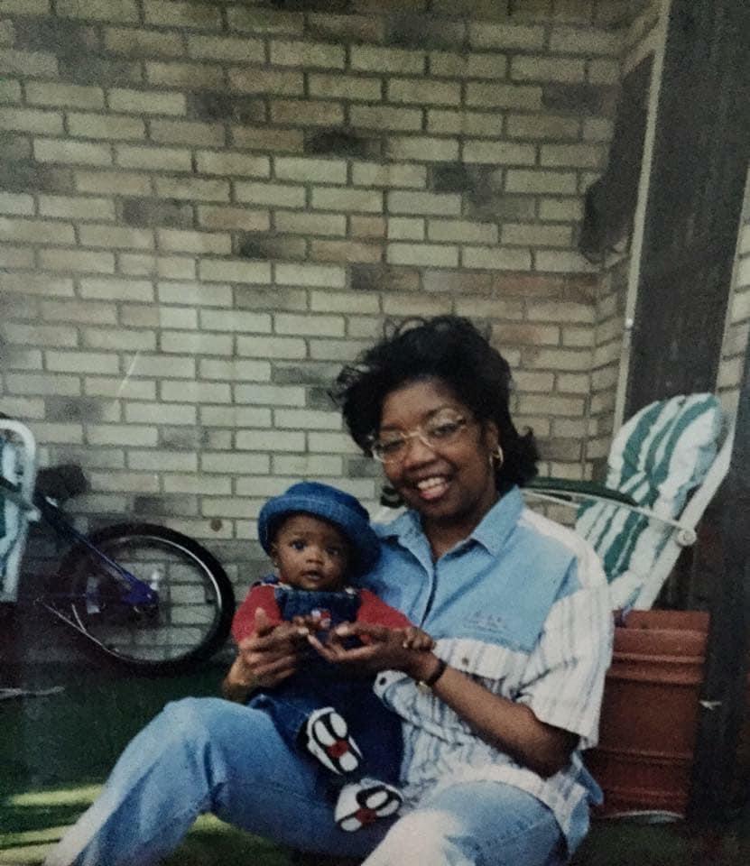 A mother sits on a porch with her child, both smiling and enjoying a sunny day together.