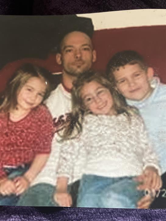 A man sits with four children, smiling and enjoying a relaxed moment in a warm setting.