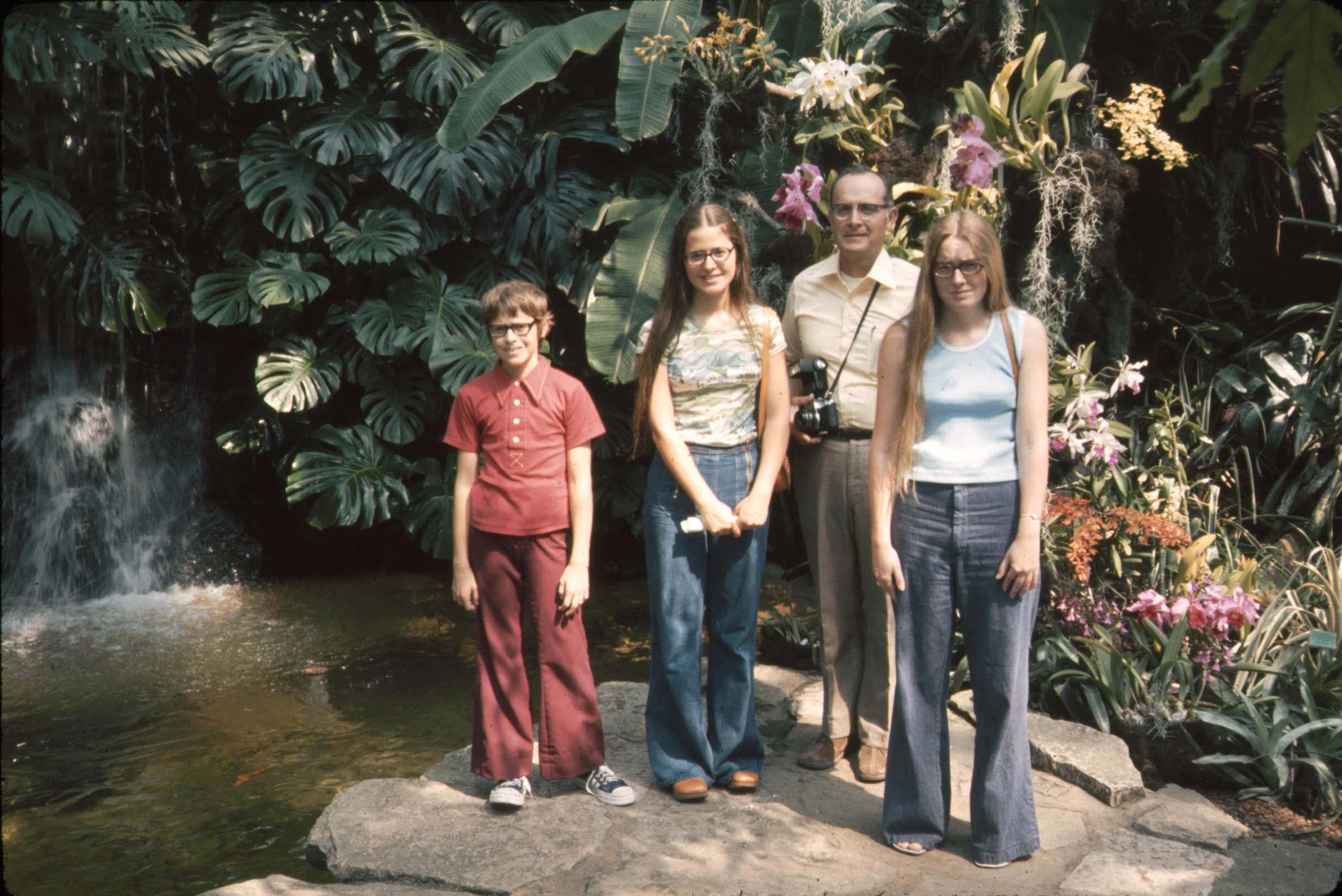 Four family members pose together at a beautiful garden with a waterfall and vibrant plants.