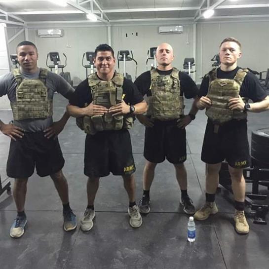 Four military members in tactical gear stand ready for workout challenges in a gym.