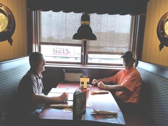 Two friends share a meal in a cozy restaurant booth, enjoying each other's company over food.