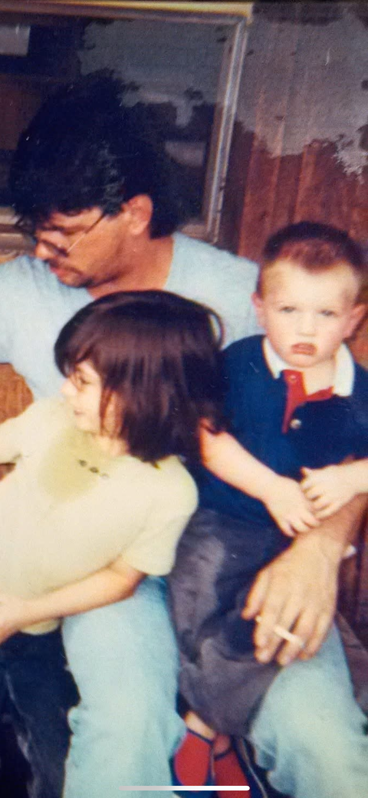 Two children sit with their father, engaging in a relaxed moment at home with a warm atmosphere.