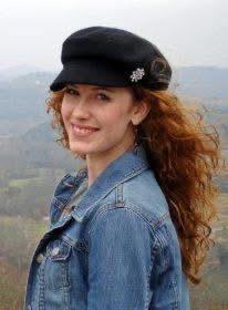 Woman with curly red hair smiles at a scenic mountainous landscape, enjoying the outdoors.