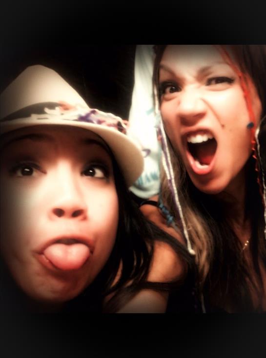 Two friends express joy and playfulness with silly faces and laughter at a social gathering.