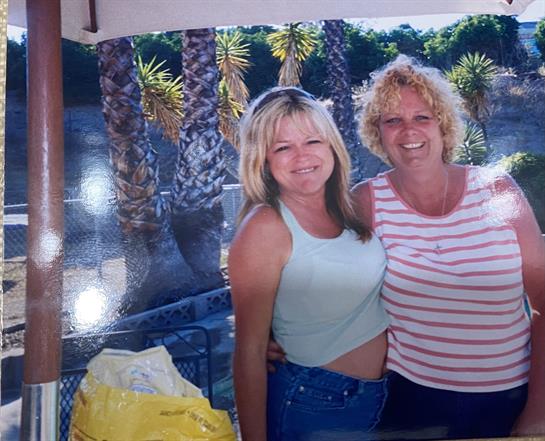 Two women stand next to each other, enjoying their time outdoors under a sunshade.