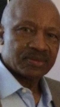 An elderly man engages in conversation, displaying a thoughtful expression while indoors.